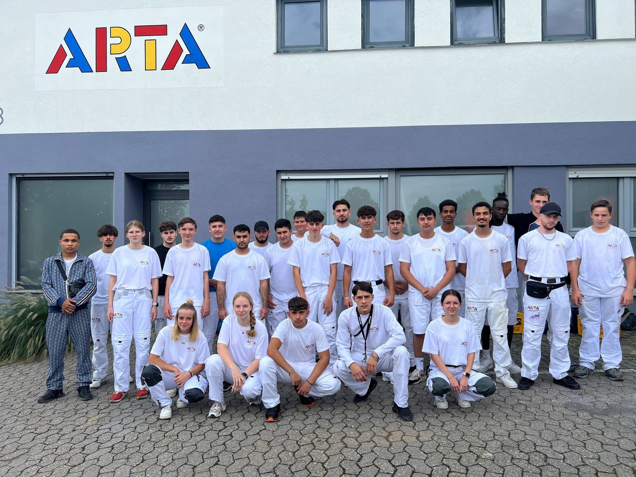 Gruppenfoto der Auszubildenden der ARTA Gruppe in weißer Malerkleidung vor dem Firmengebäude