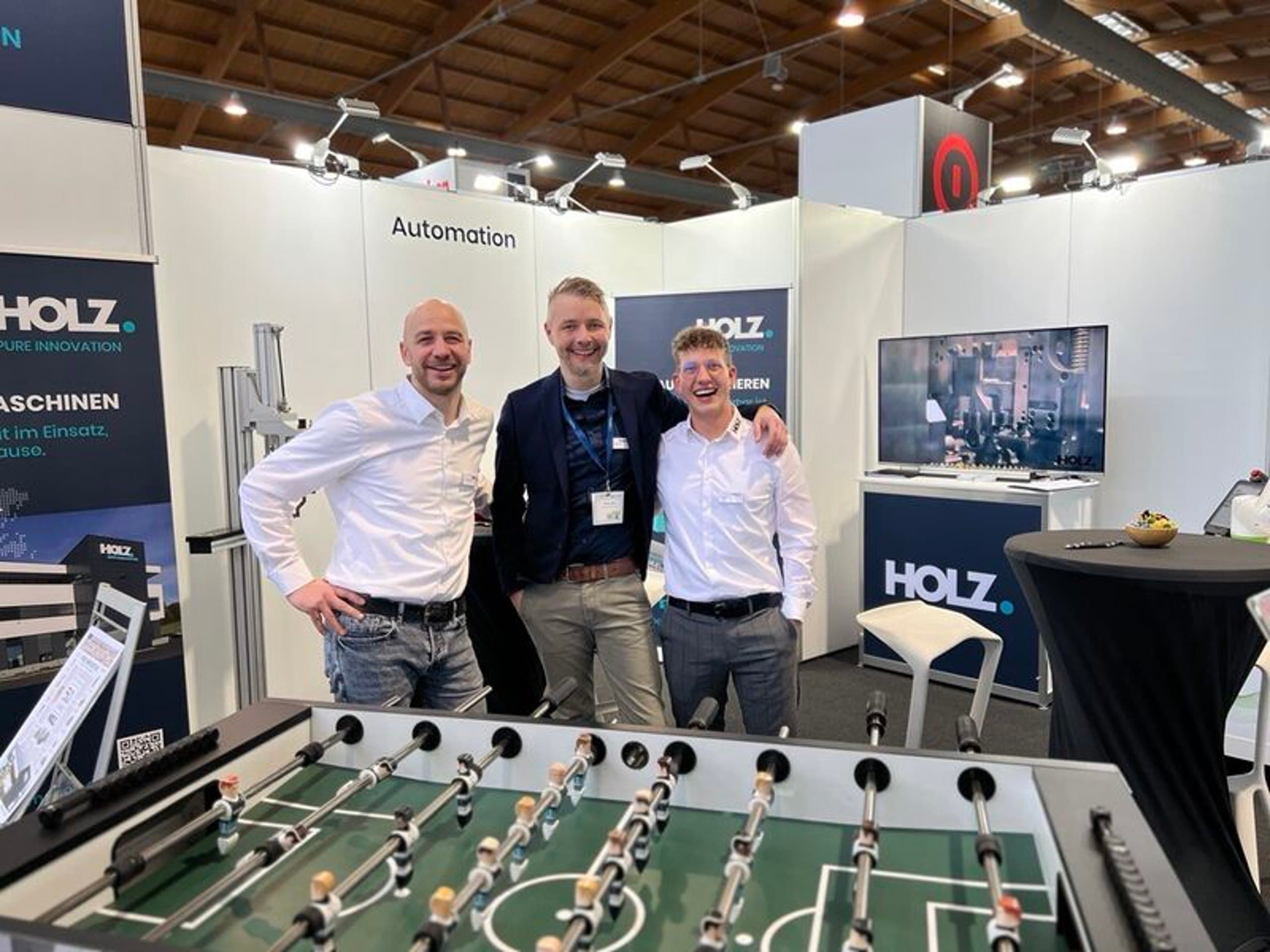 Drei Mitarbeiter der Holz Automation GmbH an einem Kickertisch auf dem Messestand des Unternehmens