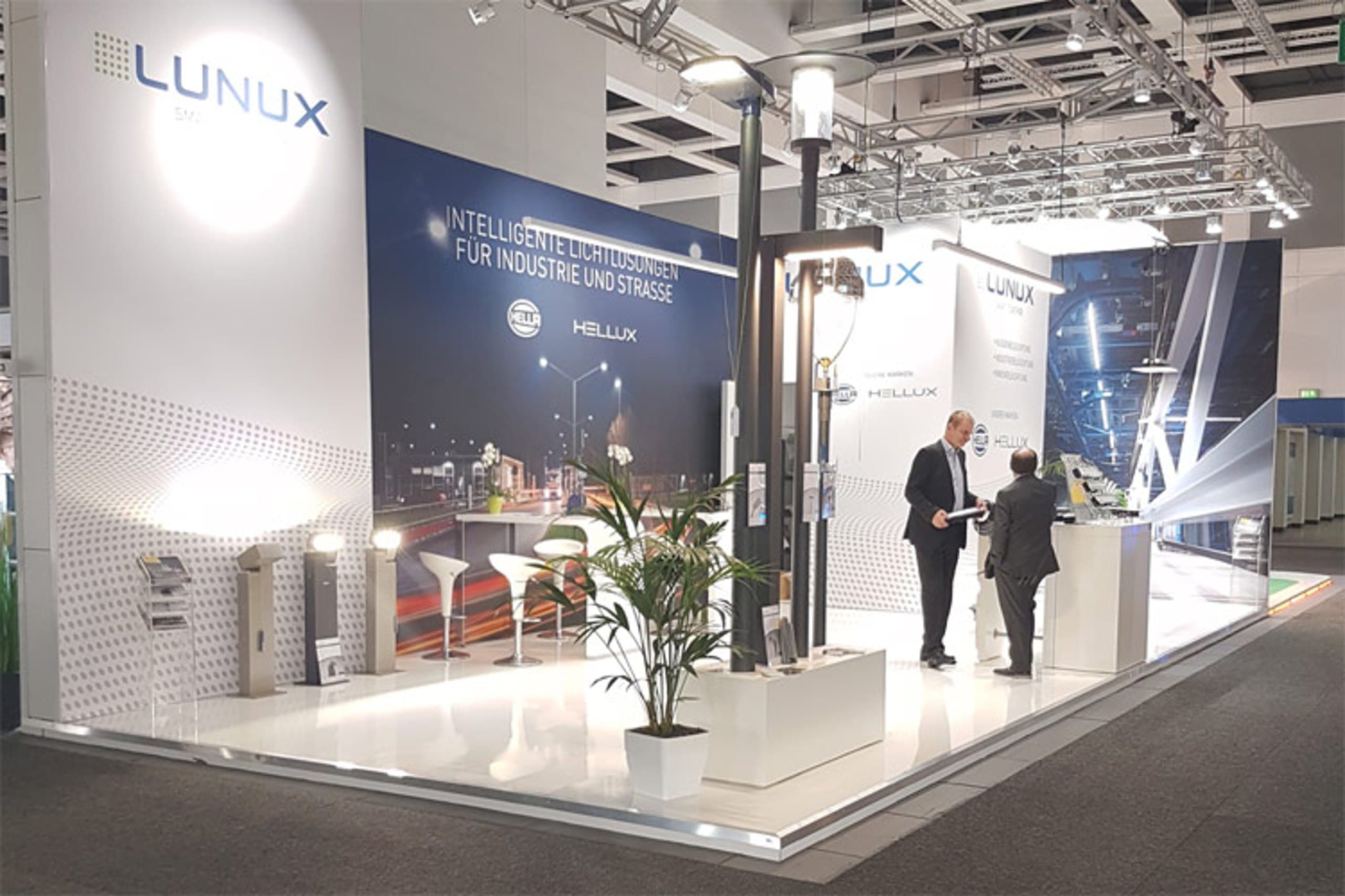 Messestand der Lunux Lighting GmbH mit beleuchteten Produktexponaten und Besuchern im Gespräch