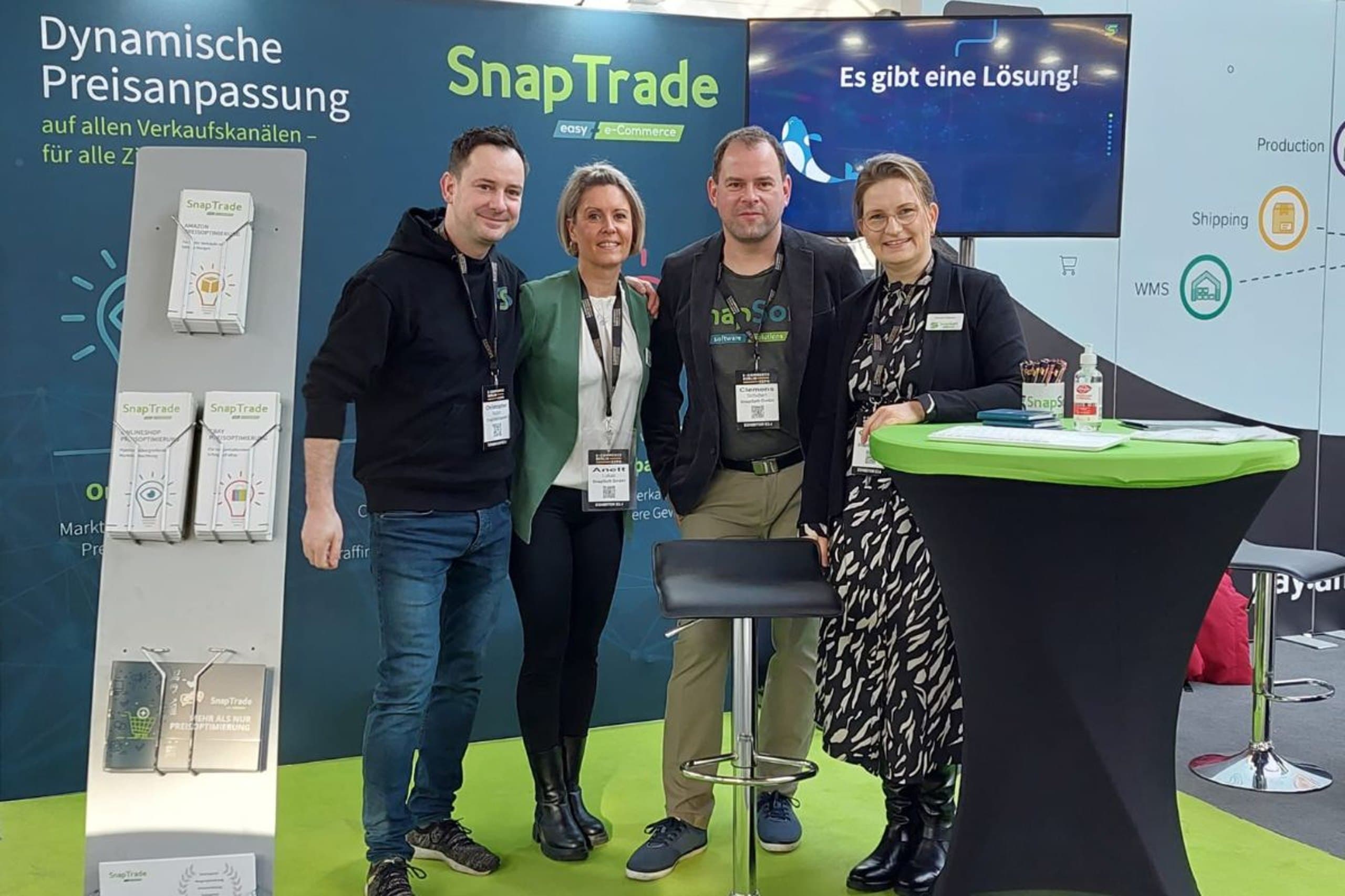 Vier Mitarbeitende der SnapSoft GmbH am Messestand vor der SnapTrade-Präsentationswand
